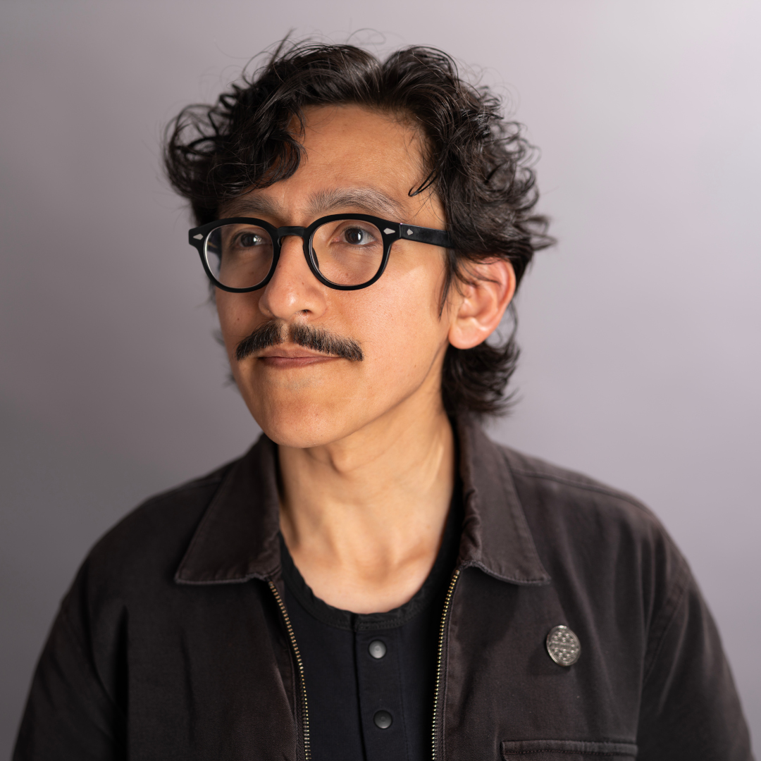 Headshot portrait of David Huerta wearing a black chore jacket over a black henley shirt.
